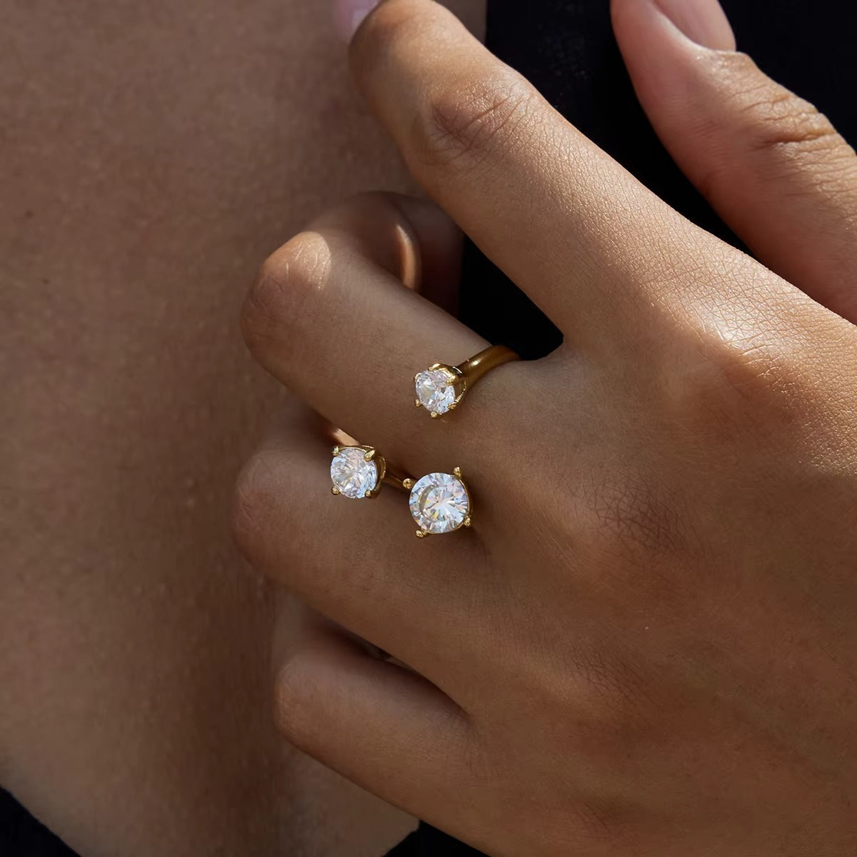 Close-up of a hand wearing the open gold Trinity RING with three clear stones, set against a dark background.