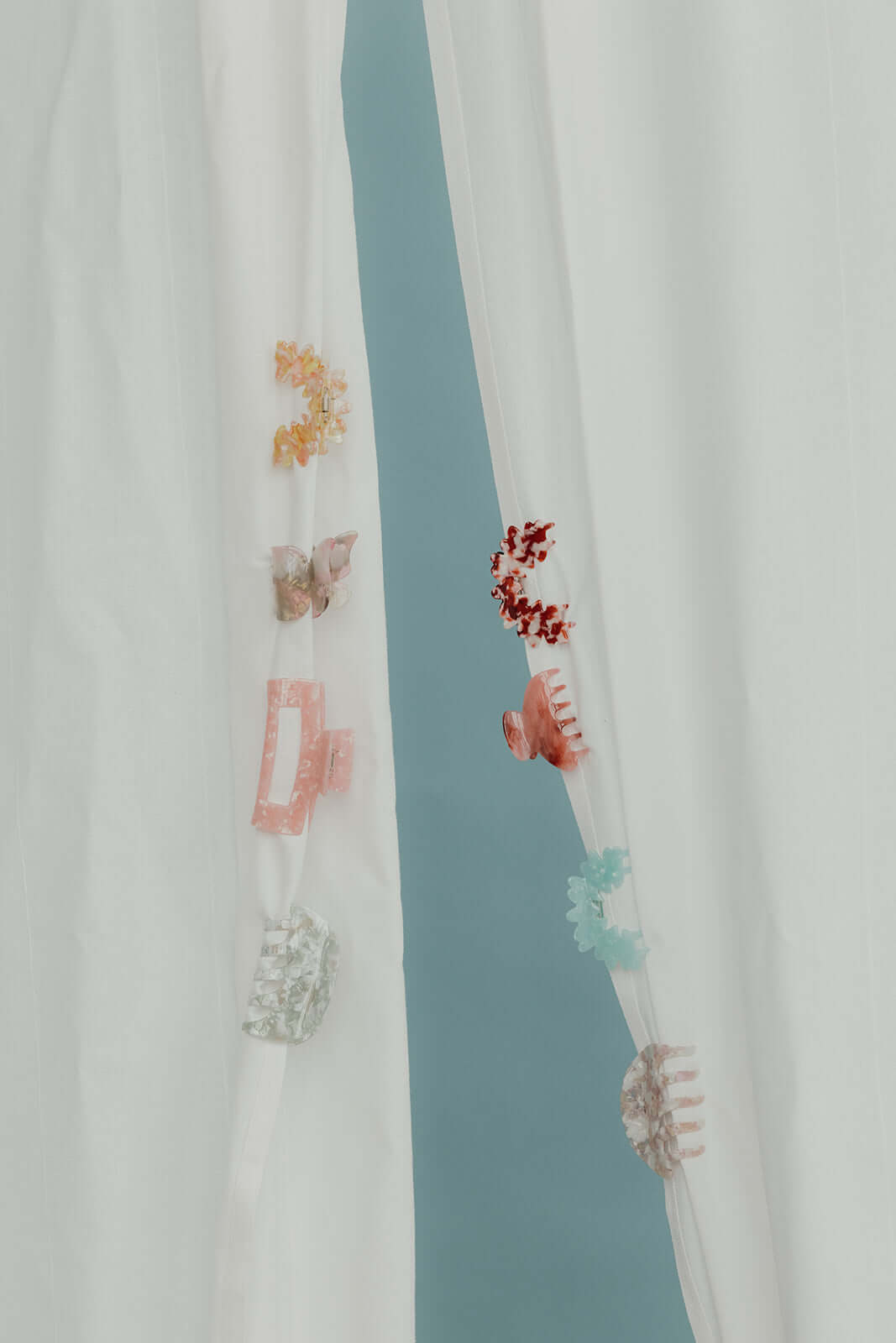 Assorted acetate hair clips in bow, butterfly and flower shapes on a sheer curtain, a generic shot not specific to True Paradise HAIR CLIP.