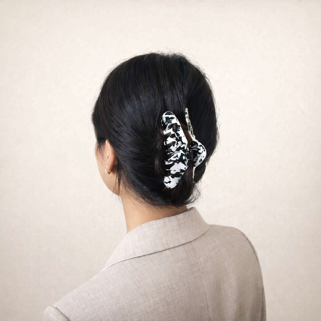 Utopia HAIR CLIP's black and white cow-print claw clip worn in a low bun, styled with a beige blazer.