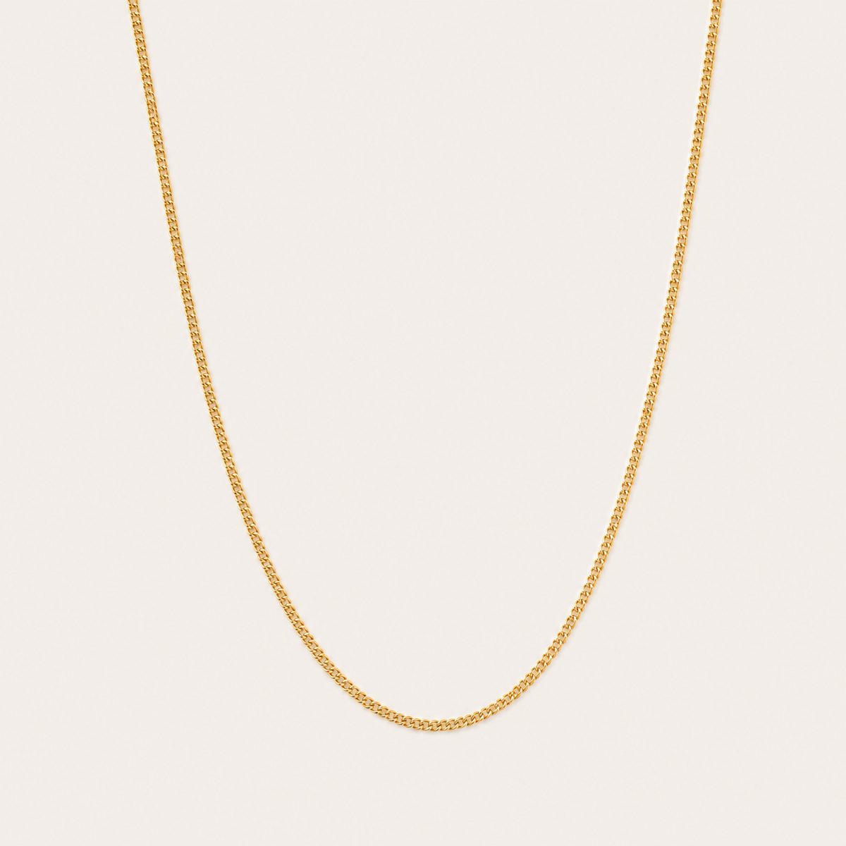 Gold curb-link chain necklace from the Vela NECKLACE design, photographed in close-up studio detail on a soft beige background.