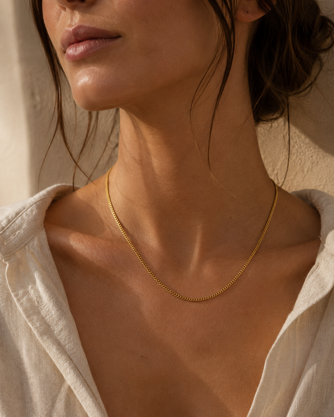 Model wears the gold Vela NECKLACE resting delicately at the neckline, paired with a cream linen shirt in warm sunlight.