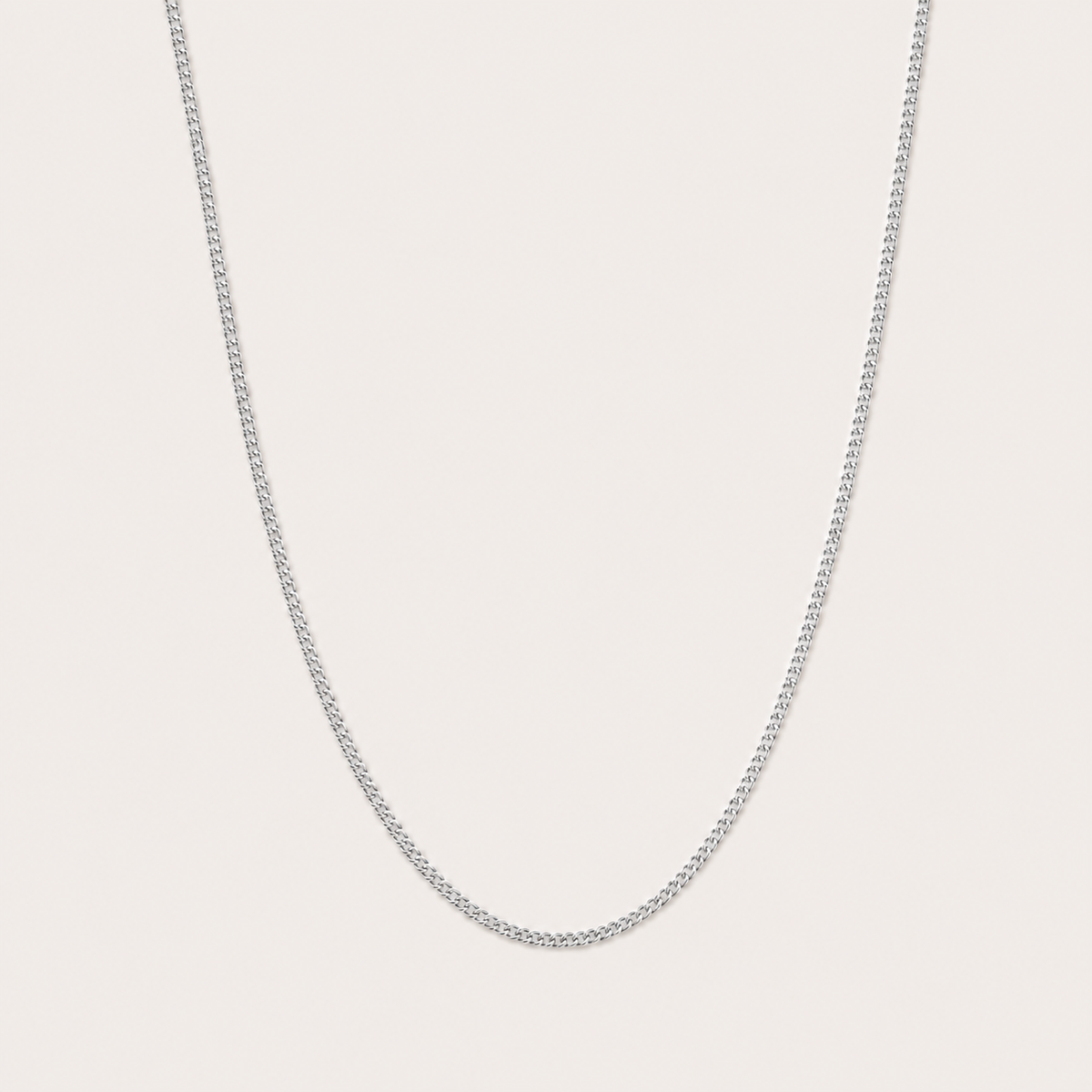 Silver curb-link chain necklace from the Vela NECKLACE design, shown in close-up studio detail on a soft beige background.