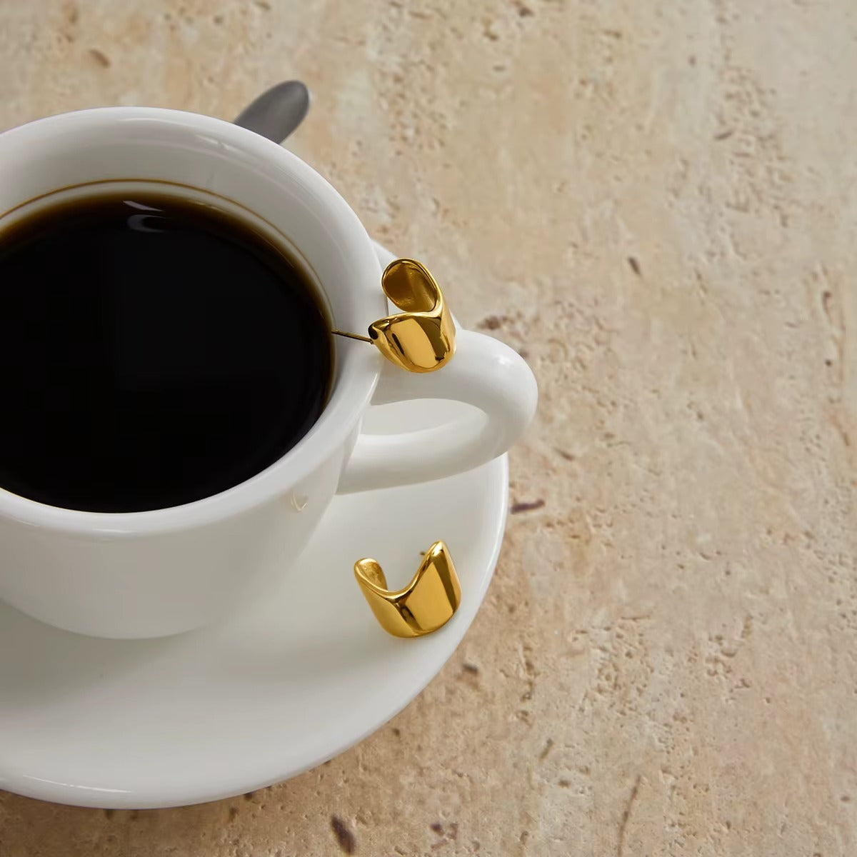 Verbier Earrings in gold perched on a coffee cup rim, the sculptural wave hoop shown up close nicely.