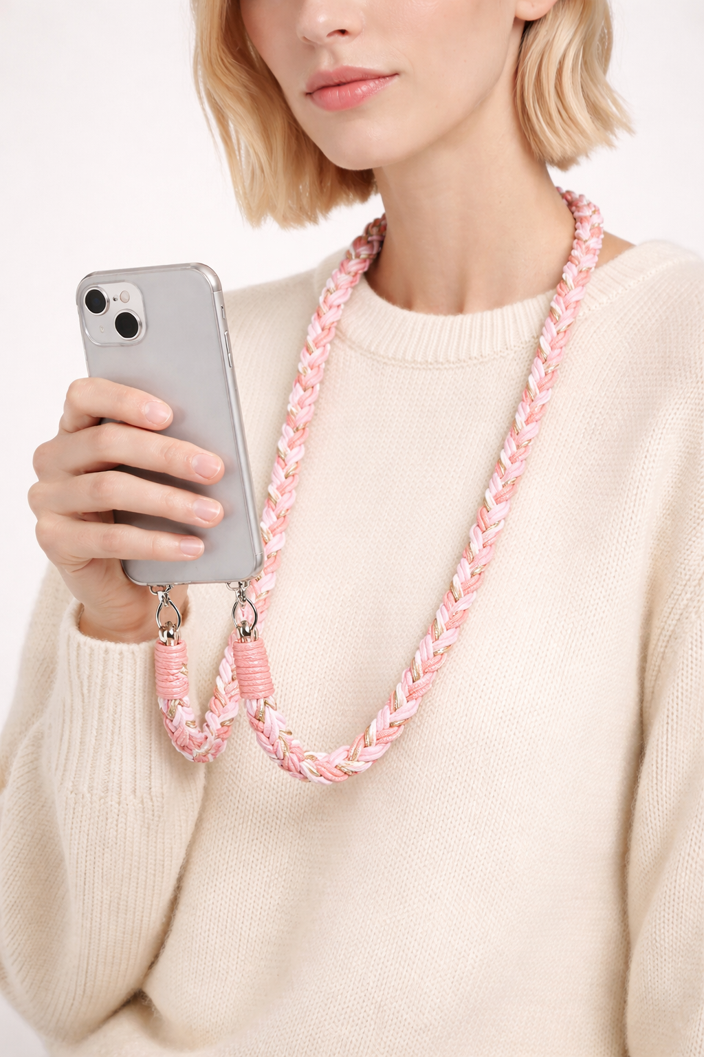 Model holds her phone by the pink braided Voyage cord worn around her neck over a cream sweater.