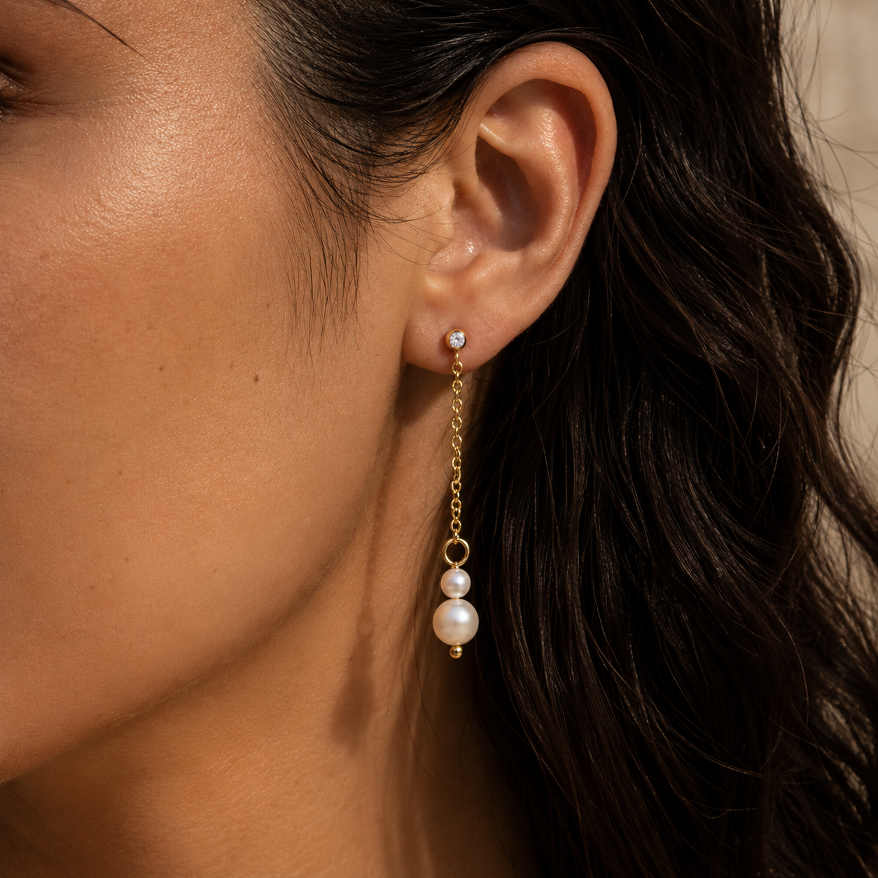 Close-up of a gold Whisper EARRINGS drop, a fine chain linking a zirconia stud to two graduated pearls.