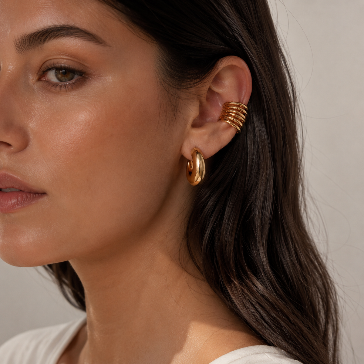 The Whitney EAR CUFF worn on the ear cartilage in close-up, a multi-band gold cuff above a chunky gold hoop earring.