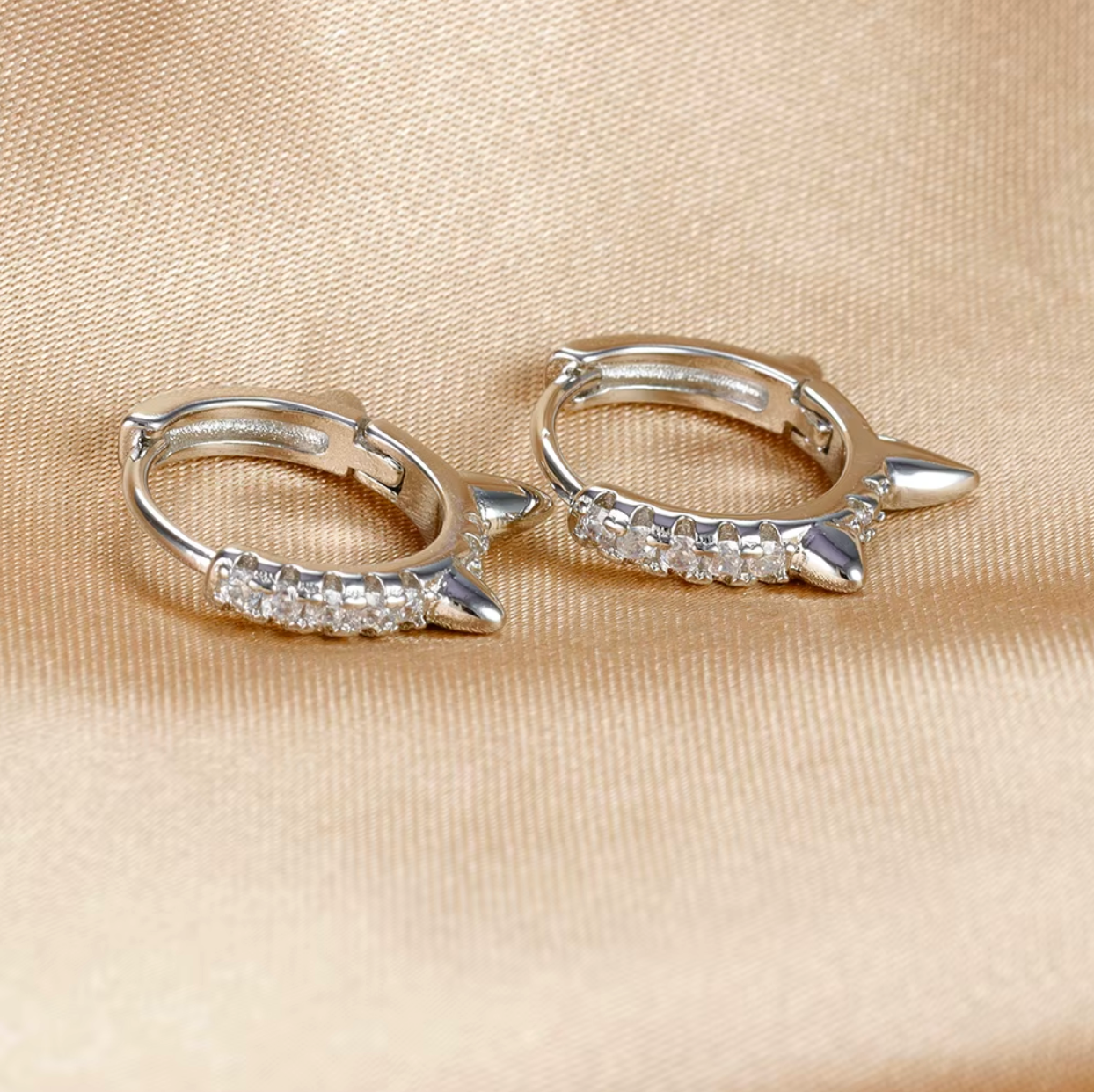 Wild Earrings in silver tone, pave spike huggie hoops resting on gold satin fabric, shown as a pair.
