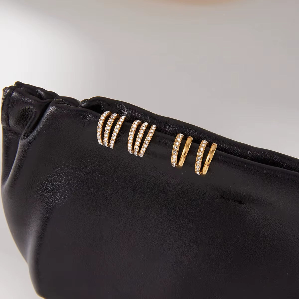 Two Wildcard Ear Cuffs laid flat on a black leather pouch, one catching light on its pave crystals, the other showing smooth gold beneath.
