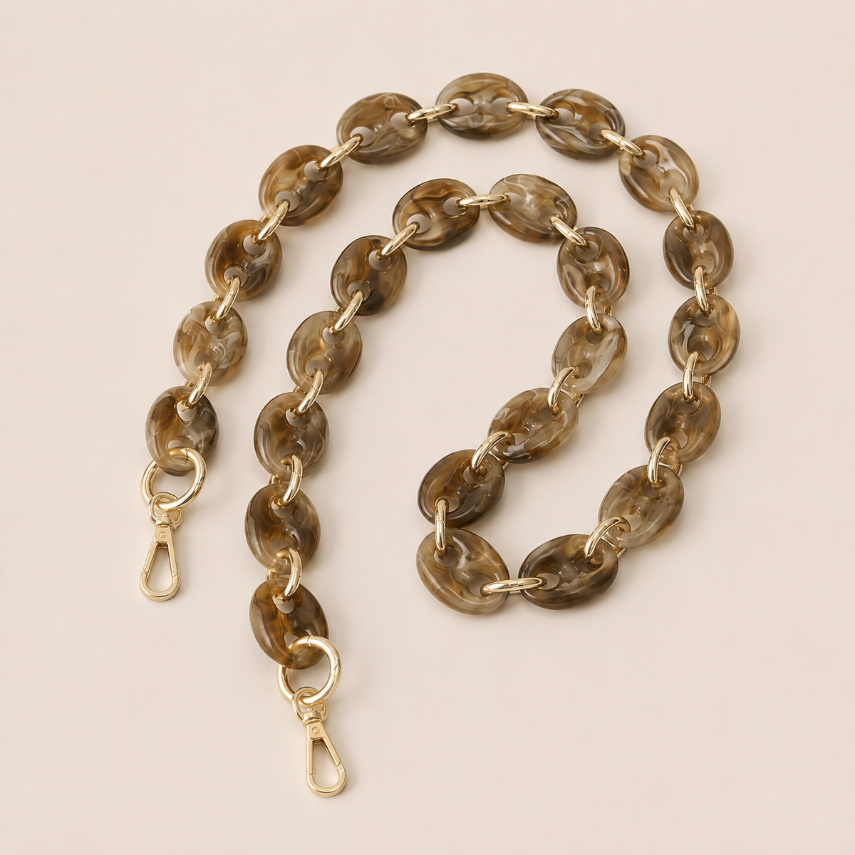 Folie à Trois Wilder long phone chain in coffee brown marbled puffed links with gold connectors, coiled on a cream background.