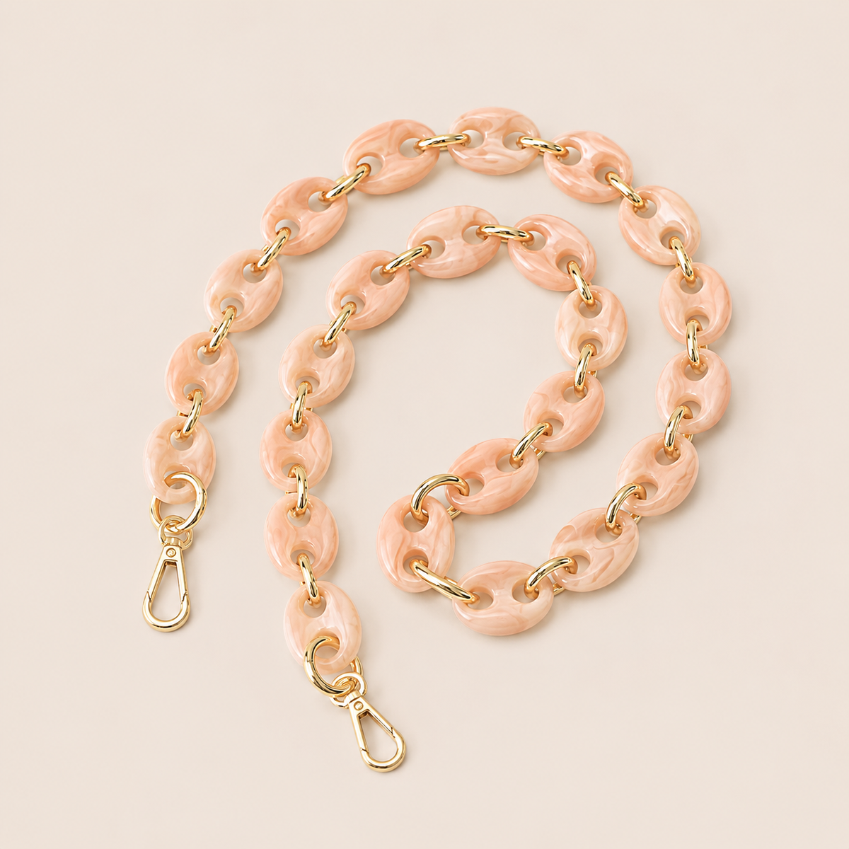 Folie à Trois Wilder long phone chain in blush pink marbled puffed links with gold connectors, coiled on a cream background.