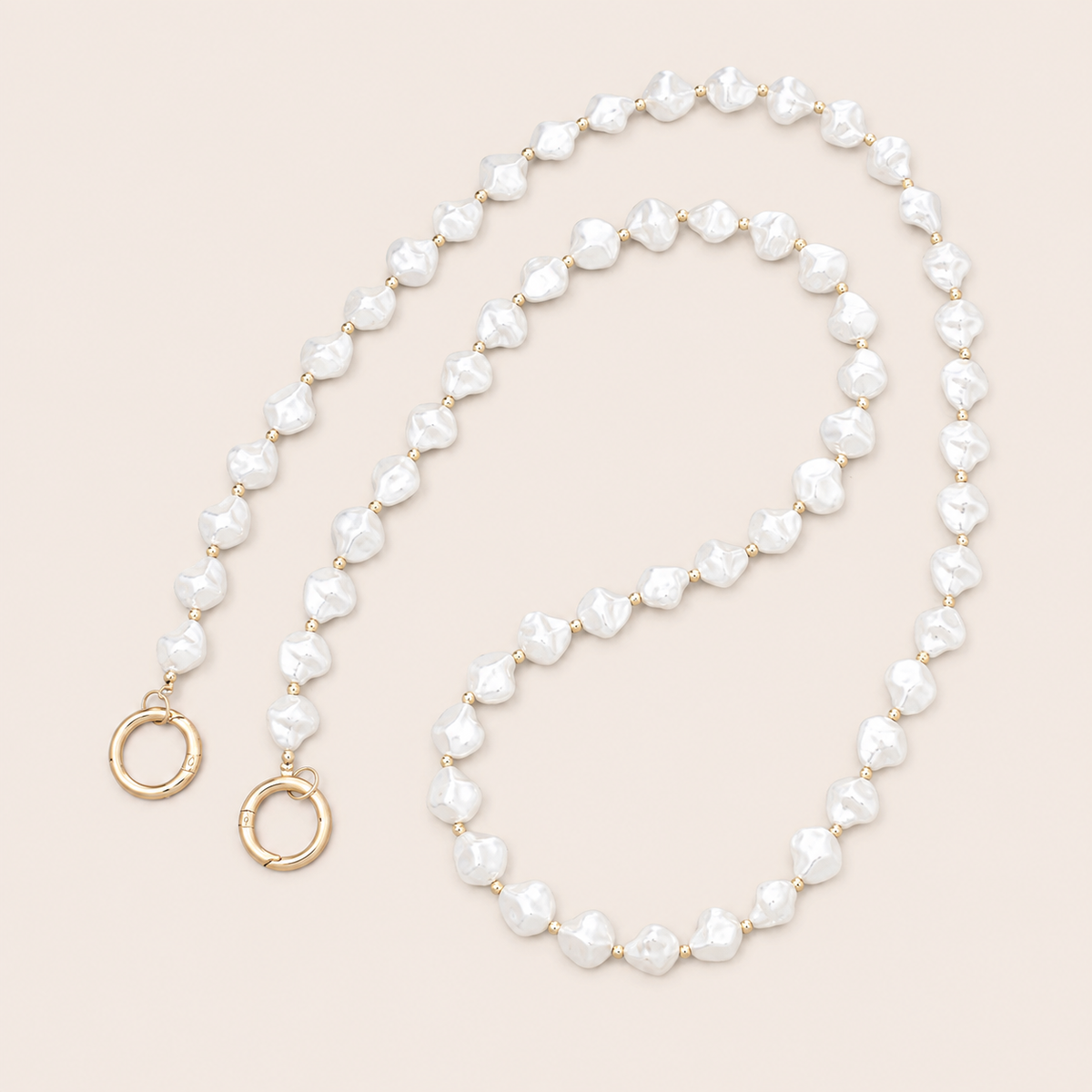 Folie à Trois Winslow Pearl wholesale phone chain in baroque white pearls with gold spacer beads and gold ring clasps, coiled on a cream background.