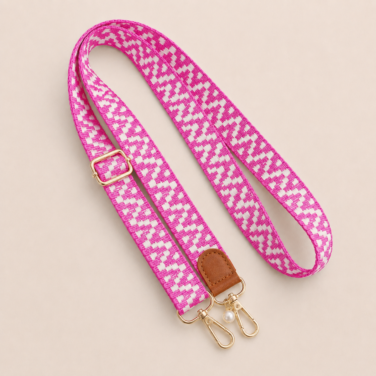 Folie à Trois Wynter long wholesale phone strap in a magenta and white zigzag weave with a tan leather tab, gold clasps and a pearl charm, coiled on a cream background.