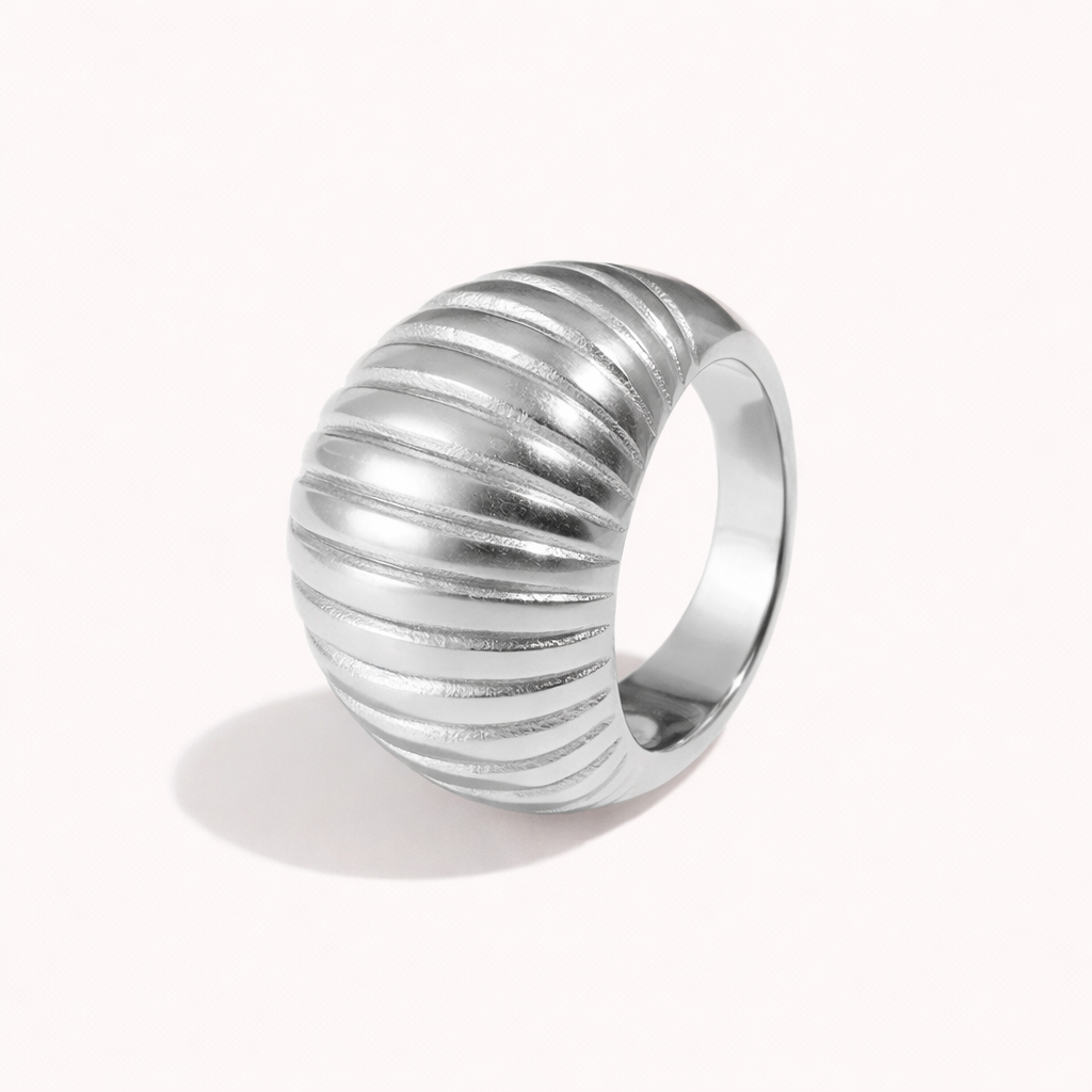 Chunky silver ring with a domed, deeply ribbed shell-like texture, shown at an angle on a cream backdrop — Zelma RING.