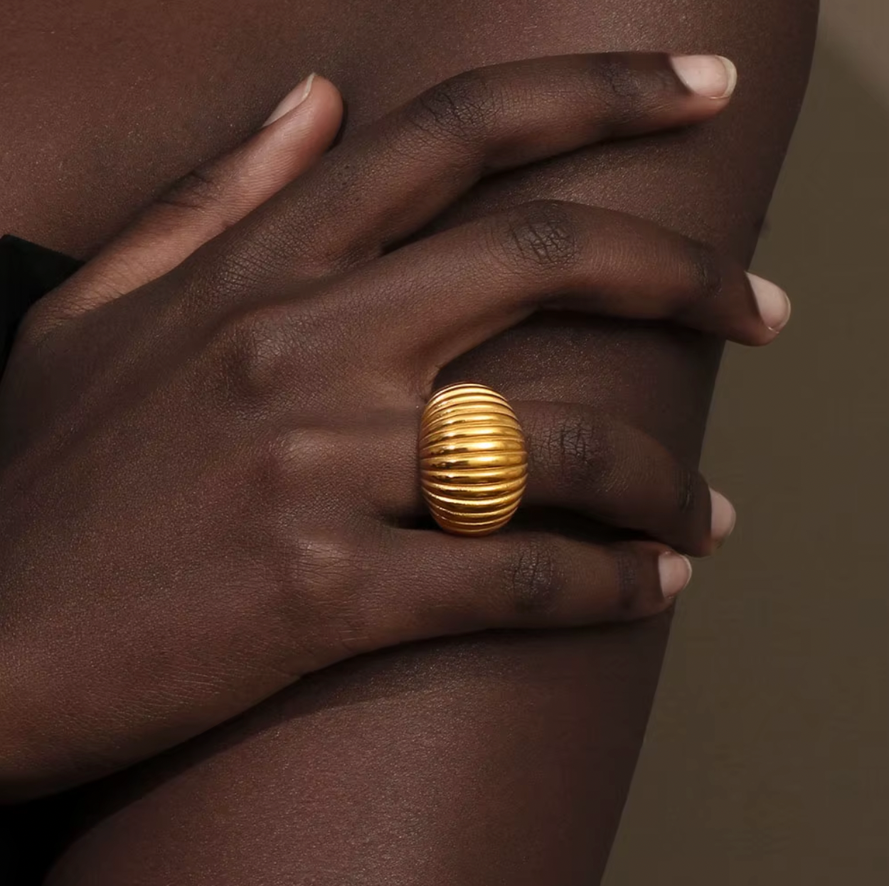 Close-up of a hand wearing the chunky gold ribbed Zelma RING, resting against bare skin.