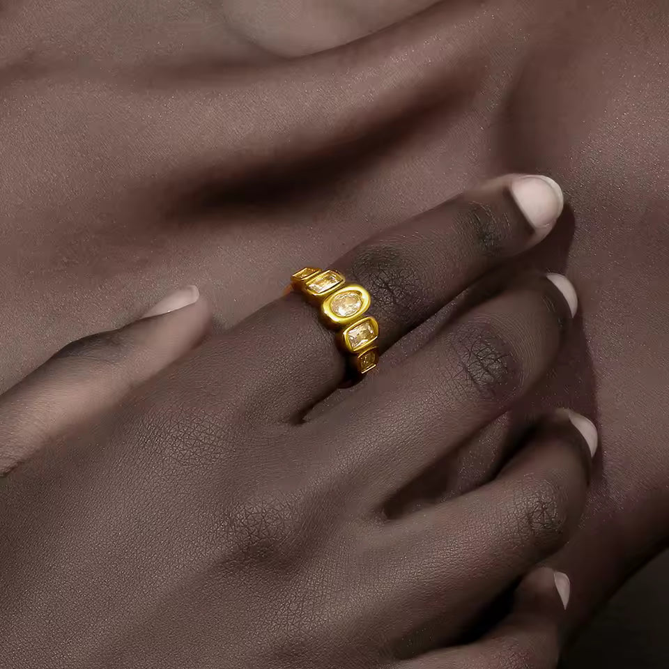 Close-up of a hand wearing the gold Zippora RING with its row of bezel-set clear stones, resting against bare skin.