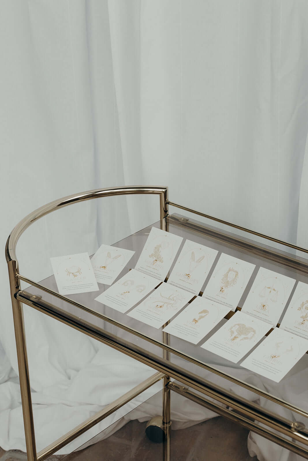All twelve Zodiac Stud Earrings horoscope cards are laid out together on a glass cart for a styled flat lay.