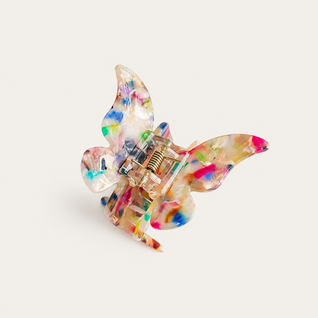 A butterfly-shaped hair claw clip made of translucent resin with multicolored paint splatters, shown on a light beige background.