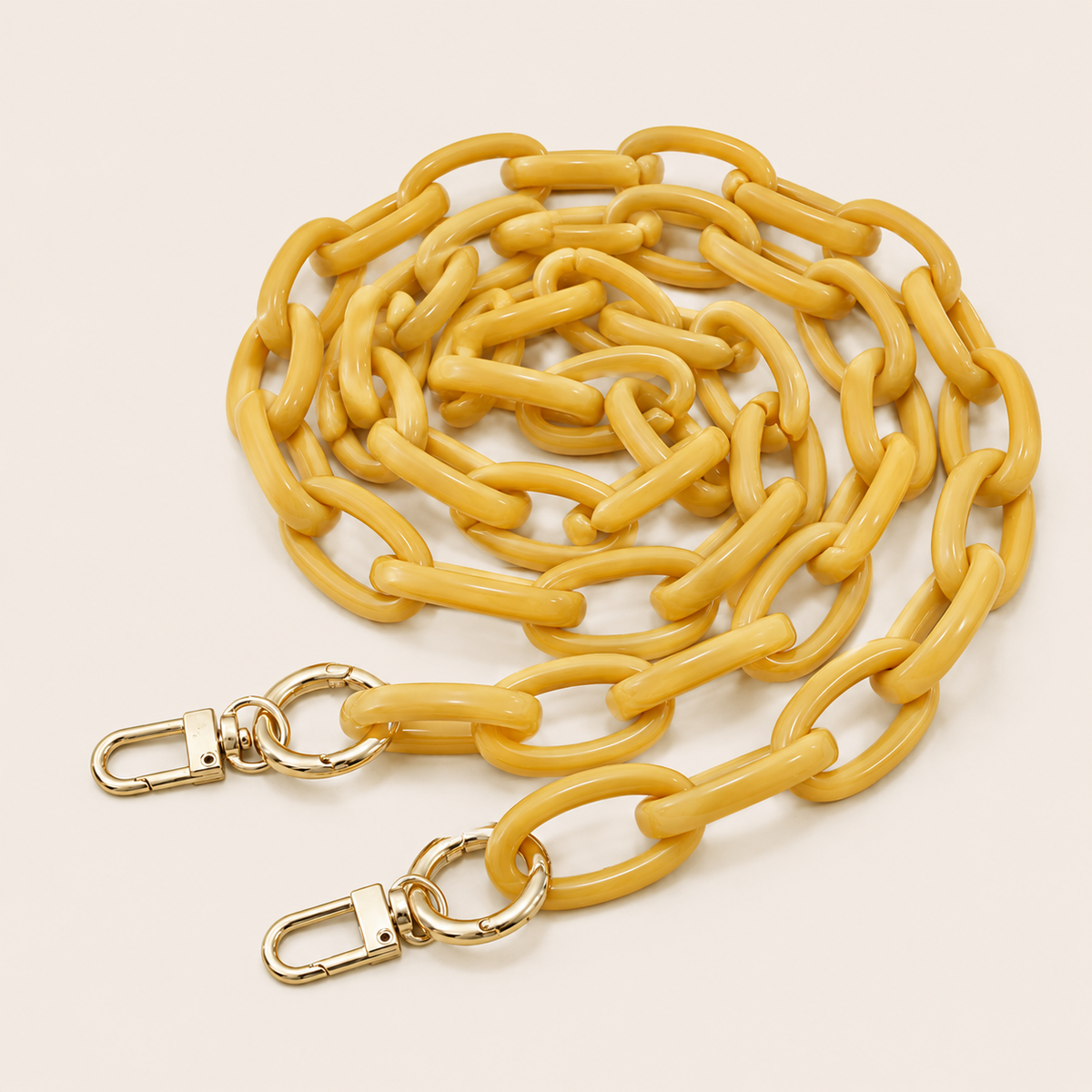 The Ember LONG PHONE CHAIN in pale yellow acrylic with gold-tone lobster clasp ends, coiled into a loop on a light beige background.