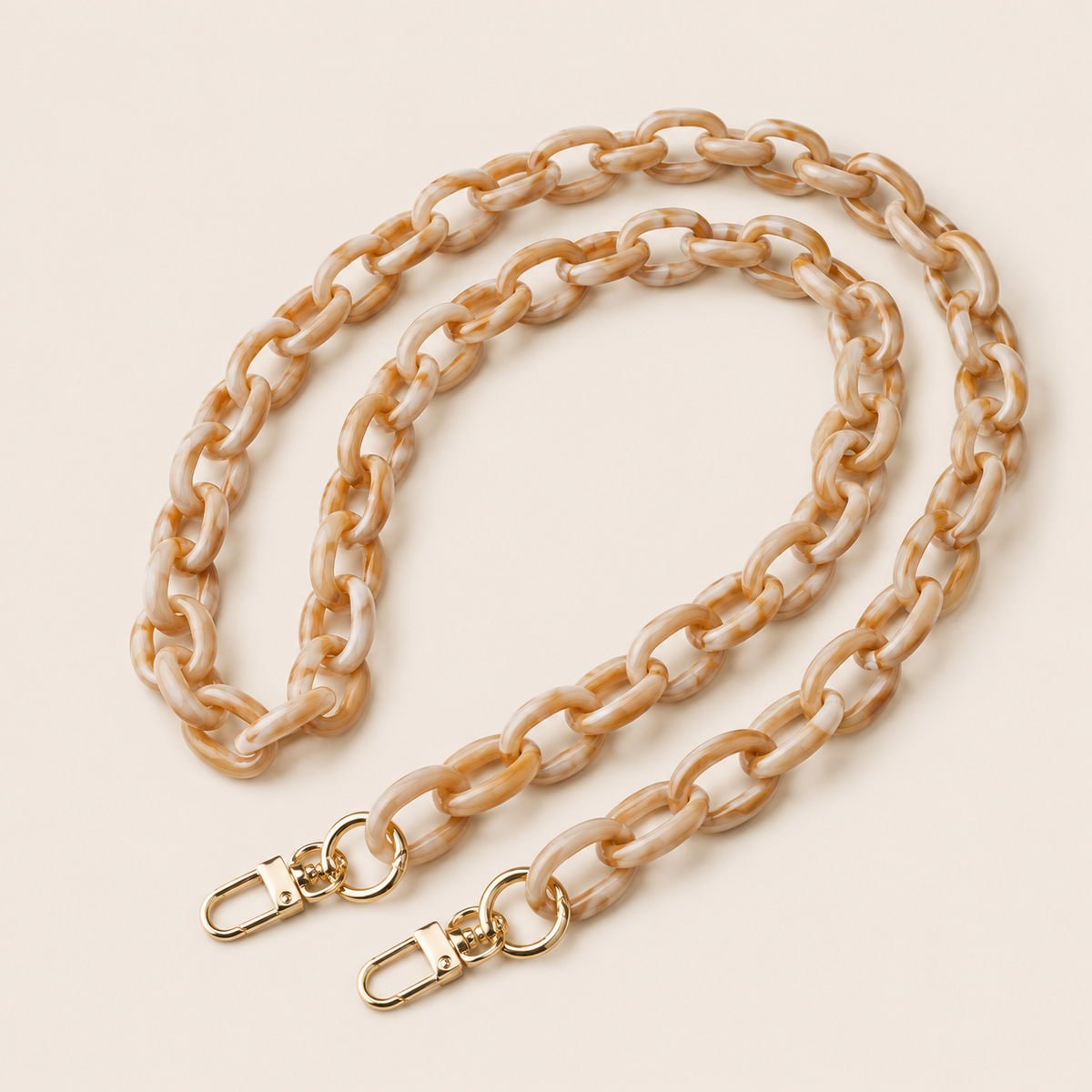 The Ember LONG PHONE CHAIN in marbled cream-and-tan acrylic with gold-tone lobster clasp ends, coiled into a loop on a beige background.