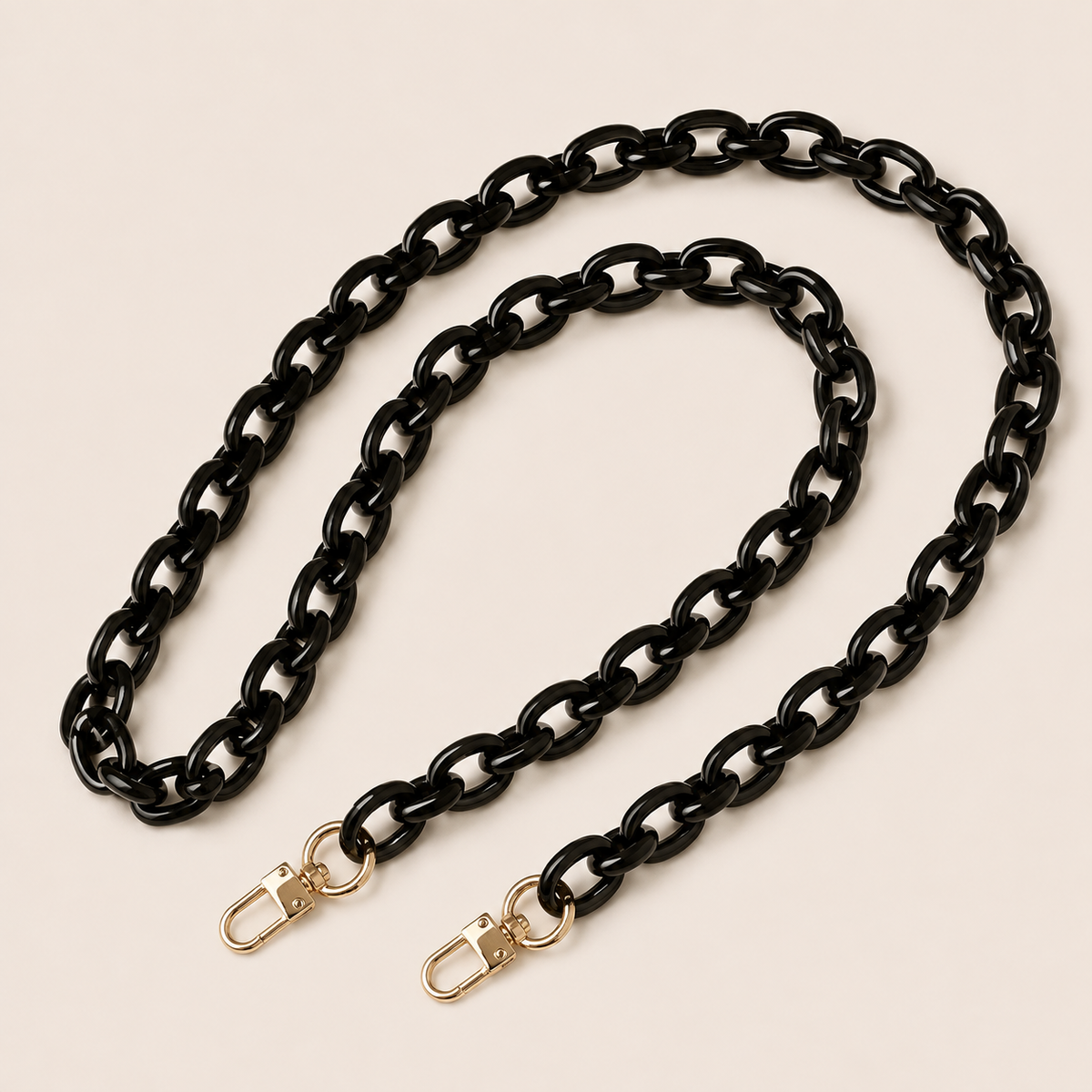 The Ember LONG PHONE CHAIN in glossy black acrylic with gold-tone lobster clasp ends, coiled into a loop on a light beige background.