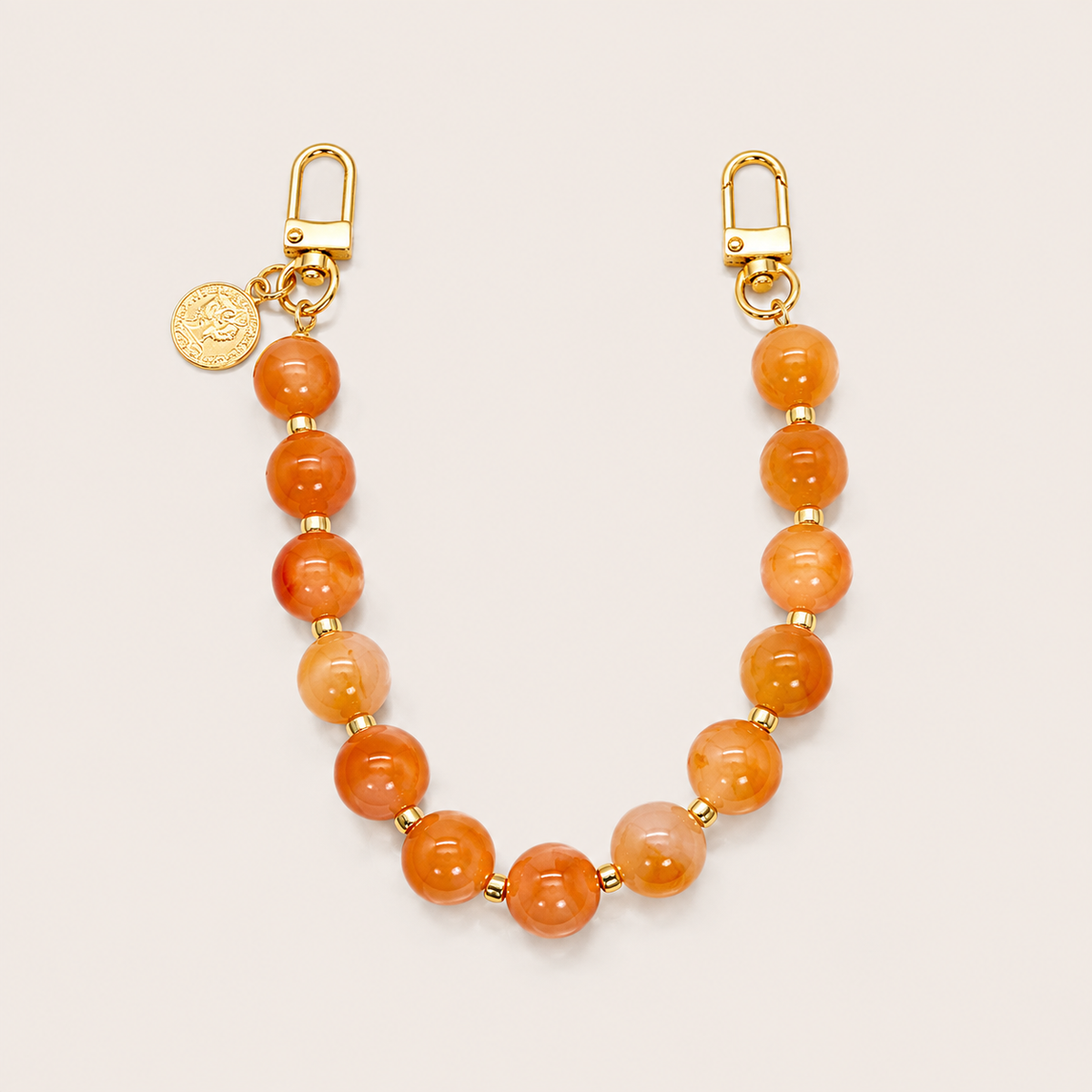 The Sable PHONE CHAIN in warm orange carnelian-effect beads with gold-tone spacers, clasps, and a coin charm.