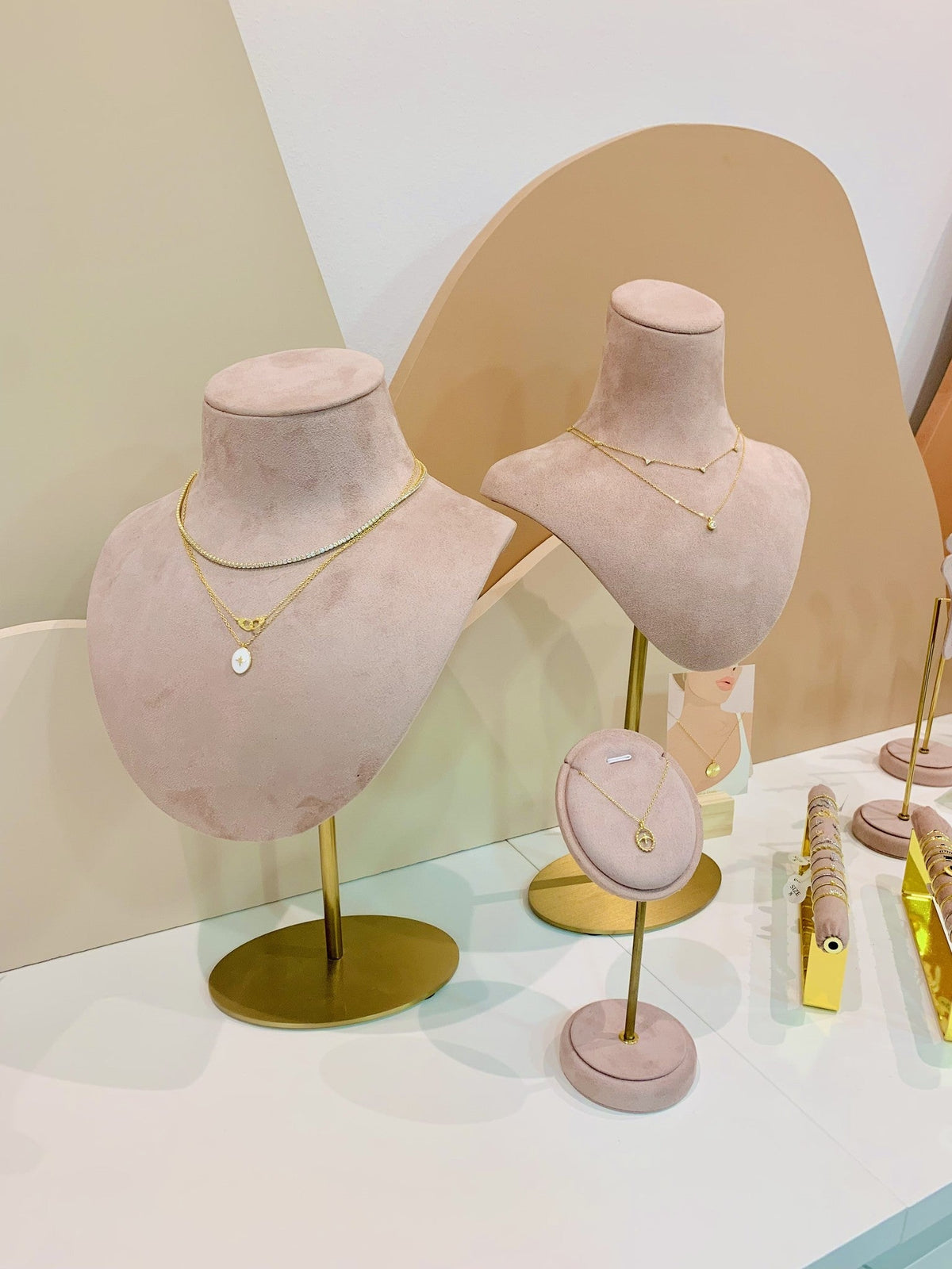 Two blush pink Mannequin Velvet DISPLAY busts on gold stands layered with gold necklaces, set up at a jewelry stand.